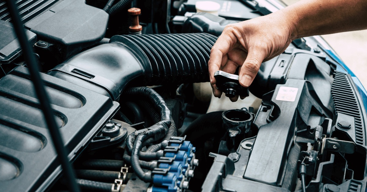 A close-up of a hand performing maintenance on a car engine, checking the oil cap, with various engine components visible, symbolizing essential car care for longevity.